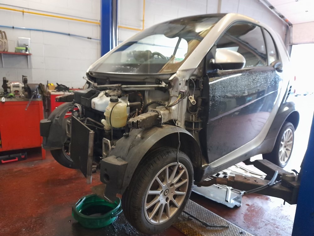A silver Smart car on the lift with its front panels removed